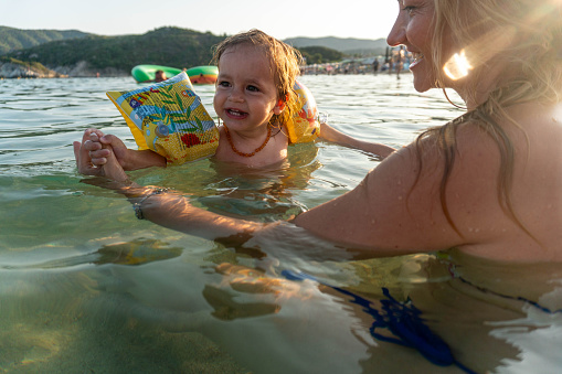 mom and little girl with water muscles in the sea swim together, laugh and enjoy