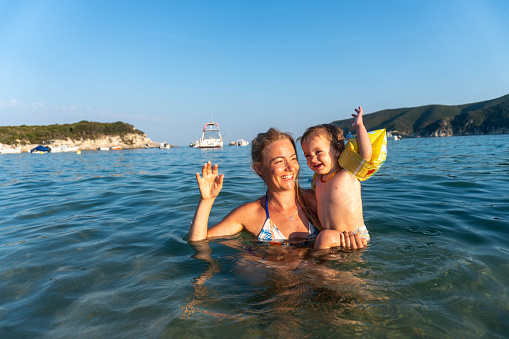 mom and little girl with water muscles in the sea swim together, laugh and enjoy and playing together