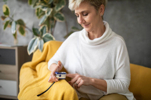 woman using a pulse oximeter at home - taking pulse oximeter medical oxygen equipment human lung imagens e fotografias de stock