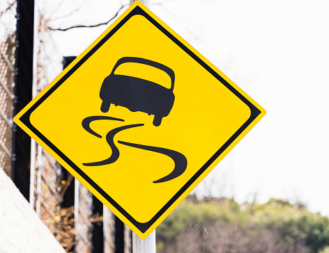 Close-up of a skidding car design on a yellow warning sign on a rural road in Japan.