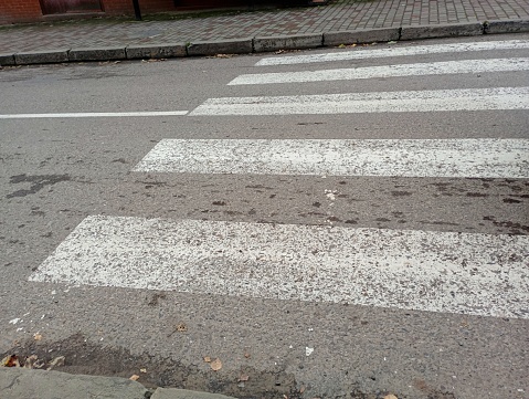 Pedestrian crossing over an asphalt road. Wide white lines for crossing the road are painted with white paint on the carriageway.