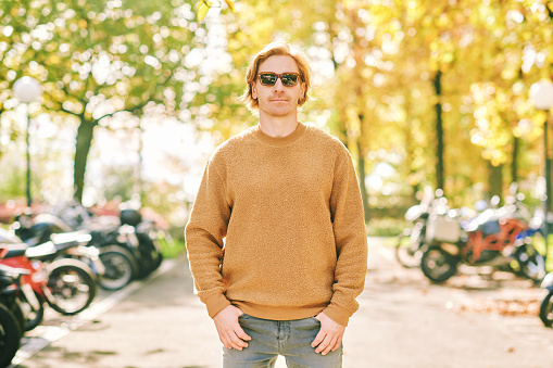 Outdoor autumn portrait of handsome young man wearing brown fuzzy fleece sweater and sunglasses