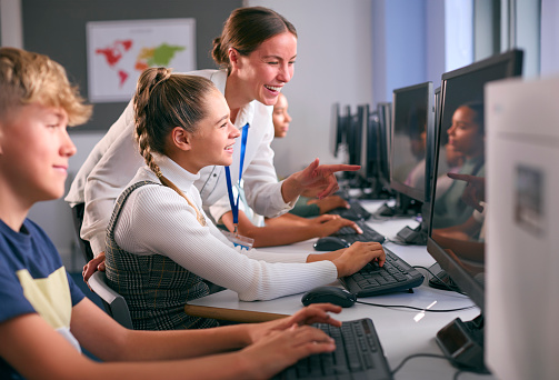 Group Of Secondary Or High School Students At Computers In IT Class With Female Teacher