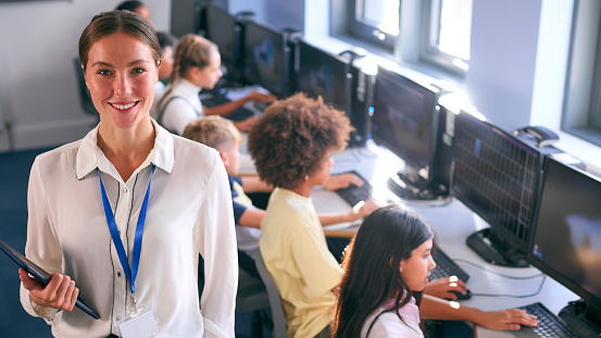 Portrait Of Female Secondary Or High School Teacher With Students At Computers In IT Class