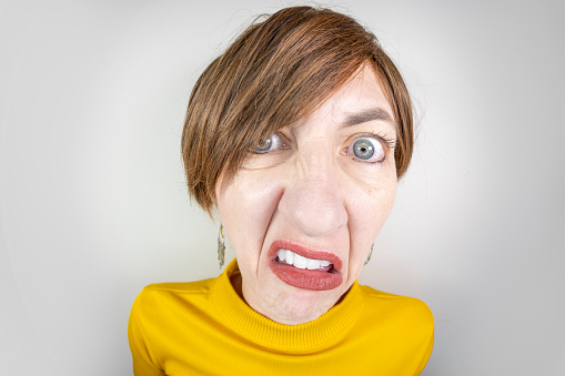 A fisheye image of a middle aged woman with short brown hair looking irritated.