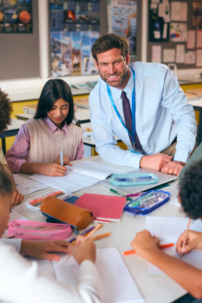 istock Male Secondary Or High School Teacher Sitting At Table Working With Students In Classroom 1822652347