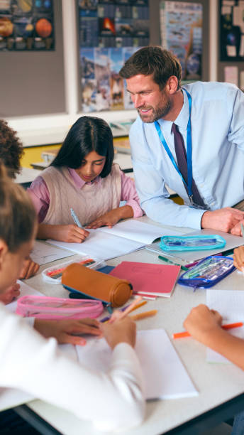 istock Male Secondary Or High School Teacher Sitting At Table Working With Students In Classroom 1822653970