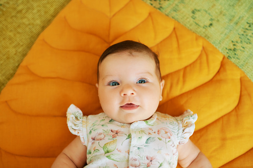 Beautiful caucasian baby laying on bed, playing with feet and smiling at camera, top view, copy space. Adorable toddler in diaper having fun alone, lying on white, laughing. Toddler, baby, infant