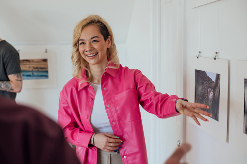 A photo exhibition opening at an art gallery in Horsley, Northumberland. The main focus is the gallery owner talking about the photographs hanging up while smiling and looking at potential buyers who are out of shot.