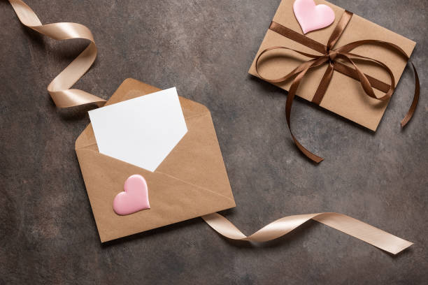 istock Open brown envelope flat lay with blank card decorated with silk ribbon and silk hearts on dark vintage background. Valentine's Day card. Top view. 1822690190