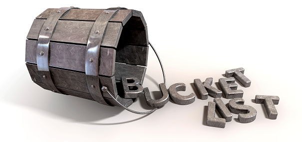 A toppled over metal vintage bucket charm with letter trinkets spilling out spelling the word bucket list on an isolated background