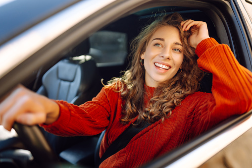 Young smiling woman driving a car drives around the city. Curly-haired woman travels by car. Lifestyle concept.