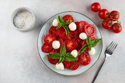 Italian caprese salad with sliced tomatoes, mozzarella, basil, olive oil on a light background. Top view. Italian food. Healthy salad. Summer food.