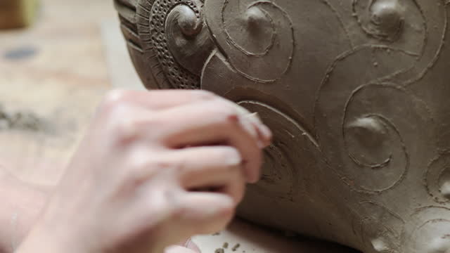 Close up latin artist woman using clay sculpting tool to design pottery work. Artistic skills, craftsmanship in action