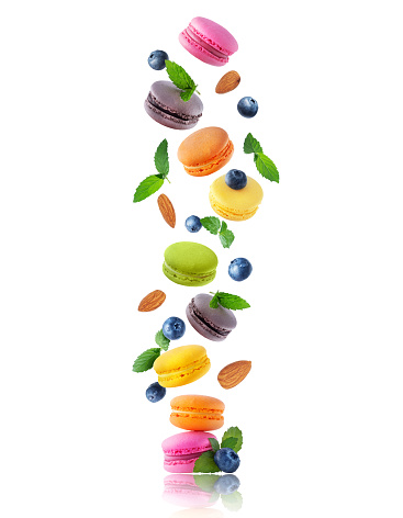 Ð¡olored macaroons with leaves of mint, blueberries and almonds in the air. Levitating colored macaroons with different flavors