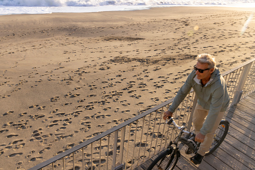 Mature man bikes up walkway above beach, Liguria