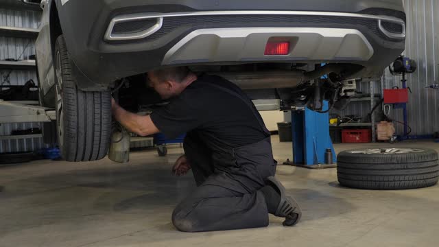A mechanic repairs a car at a service station. The car is on the lift.