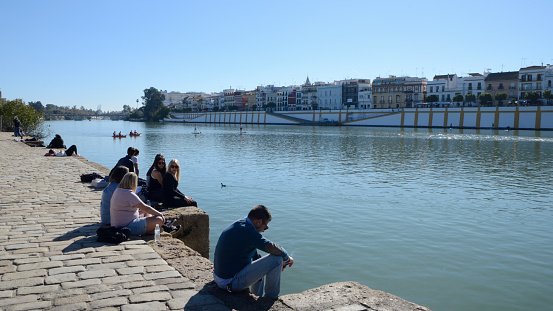 Seville, Spain - November 25, 2023: People at the banks river Guadalquivir in front of Triana quarter in Seville, Spain.