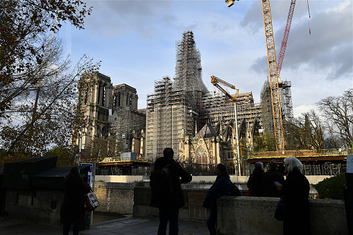 Paris, France-11 29 2023: Silhouettes of walkers on the banks of the Seine watching the progress of work on Notre-Dame Cathedral with the installation of the spire, Paris, France.