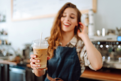 Portrait of a smiling female barista with a takeaway drink standing behind a bar counter. Business concept, food and drinks.