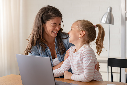 A cheerful mother and daughter engage in a video call over a laptop computer, sharing smiles and moments of connection