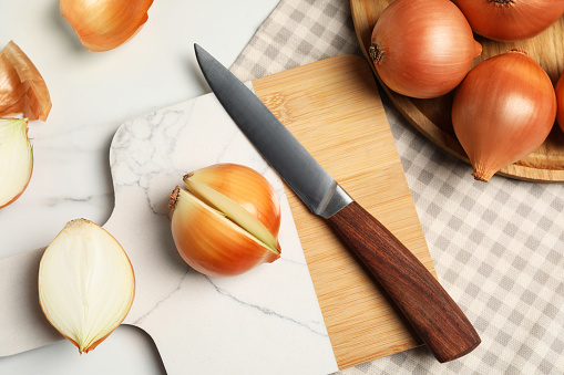 Whole and cut onions with knife on white marble table, flat lay