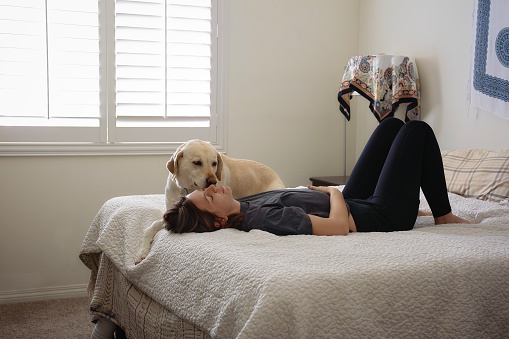 A woman is laying on her back on a bed with her dog while looking up at the ceiling.