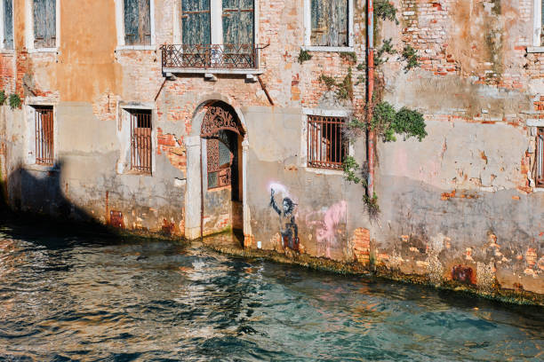 Venice canal houses, gate and the graffiti by Banksy, the shipwrecked migrant child stencil street art Venice, Italy - November 9 2023: Venice canal waters, gate and graffiti by Banksy, the shipwrecked migrant child stencil street art banksy stock pictures, royalty-free photos & images
