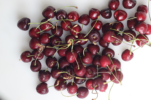 Vibrant, succulent cherries nestled together in a delightful cluster, showcasing rich hues of red against lush green stems. Freshness captured in a single frame. Shot on white backgrounds