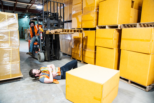 A man in pain on the ground after being hit by a forklift in a warehouse.