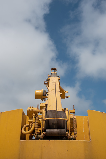 Details of a yellow industrial crane against blue cloud sky. Heave duty machinery for construction outdoor.
