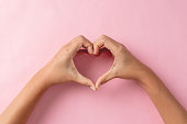 Heart shape created from young woman's hands on pastel pink background