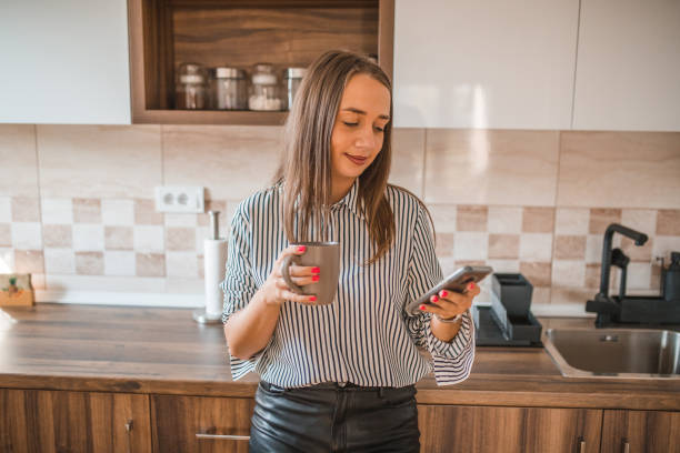 istock Business woman using mobile phone while resting drinking coffee in kitchen of hotel room 1822801391