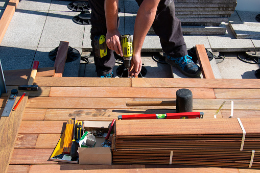 Ipe wood terrace deck construction, view of carpenter hands with a power screwdriver and woodworking tools while installing a deck, tropical hardwood decking