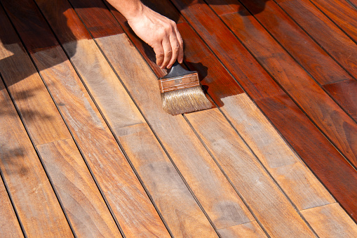 Ipe hardwood deck annual refreshing, worker's hand is oiling terrace decking with a painting brush after sanding