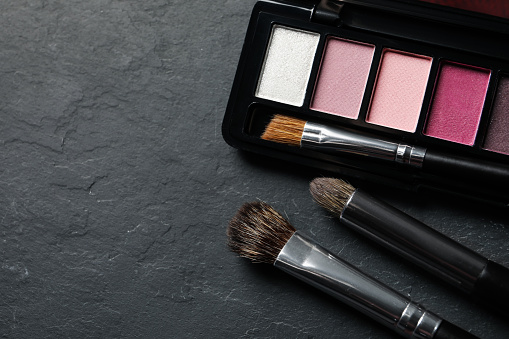Beautiful eye shadow palette and brushes on dark grey textured table, flat lay. Space for text