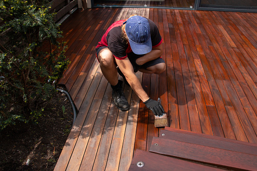 Hardwood deck oiling, trade worker applying terrace oil with a brush, decking renovation and nourishing