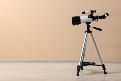 Tripod with modern telescope near beige wall. Space for text