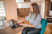 Smiling business woman using digital tablet during business trip. She is in a hotel room working remotely