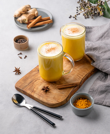 Turmeric golden milk latte with spices and honey. Detox, immunity boosting, anti-inflammatory, healthy, cozy drink in a glass cup on a wooden board on a light background.