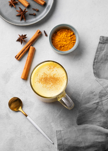 Turmeric golden milk latte with spices and honey. Detox, immunity boosting, anti-inflammatory, healthy, cozy drink in a glass cup on a light background. Top view.