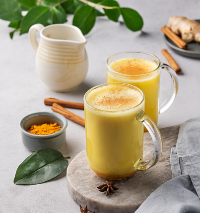 Turmeric golden milk latte with spices and honey. Detox, immunity boosting, anti-inflammatory, healthy, cozy drink in a glass cup on a light background close up.
