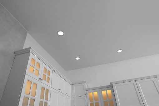 Ceiling with modern spot lamps and furniture in stylish kitchen, low angle view
