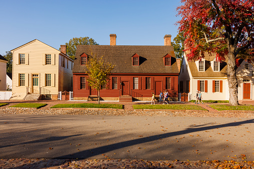 Colonial Williamsburg, Virginia, USA — October, 2023: row colonial style houses and trees line the street in Historic District of the city in autumnal day. Family strolling along the street