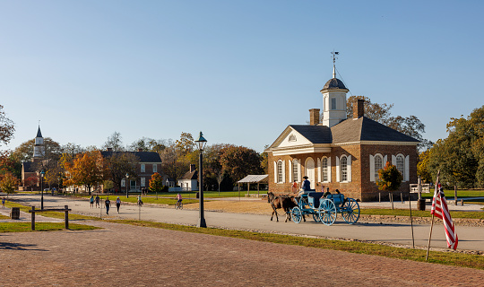 Colonial Williamsburg, Virginia, USA — October, 2023: A horse-drawn carriage rides in front of the courthouse on E Duke of Gloucester in Historic District — living history museum for tourists. Bruton Parish Episcopal Church shown in the distance