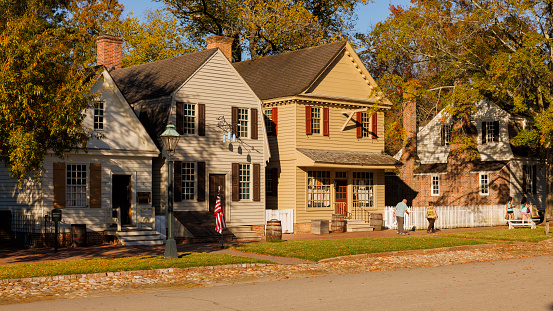 Colonial Williamsburg, Virginia, USA — October, 2023: row colonial style houses line the street in Historic District of the city. Senior couple of man with walking cane and woman walking along the street