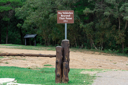Inscription on wooden plank with No Vehicles beyond this point in park, warning sign.