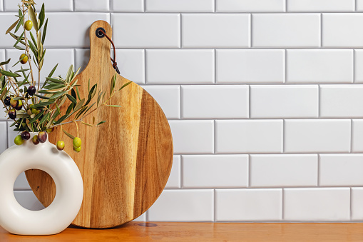 Olive branches in a vase and wooden board over the white tile wall, modern kitchen interior