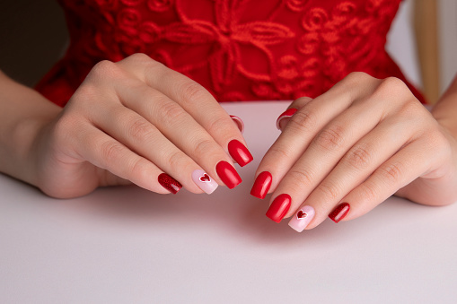 Beautiful female hands with red manicure nails, hearts and Valentine's day design