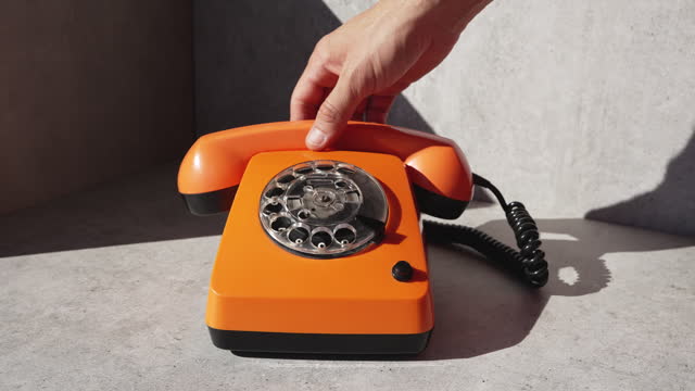 Using an old fashioned orange vintage rotary telephone. Orange retro phone with harsh shadows